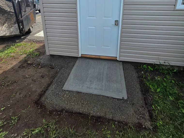 Après : la dalle de béton finie devant la même porte de côté, bordée de gravier