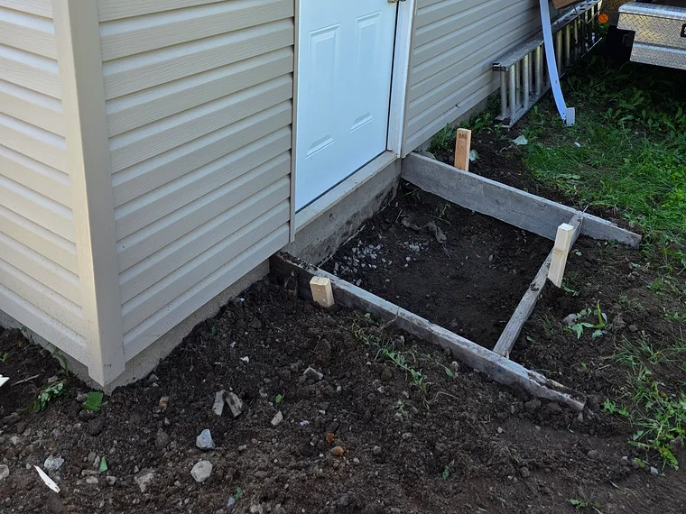 Avant : le sol excavé devant la porte de côté, coffrage de bois posé sur la terre